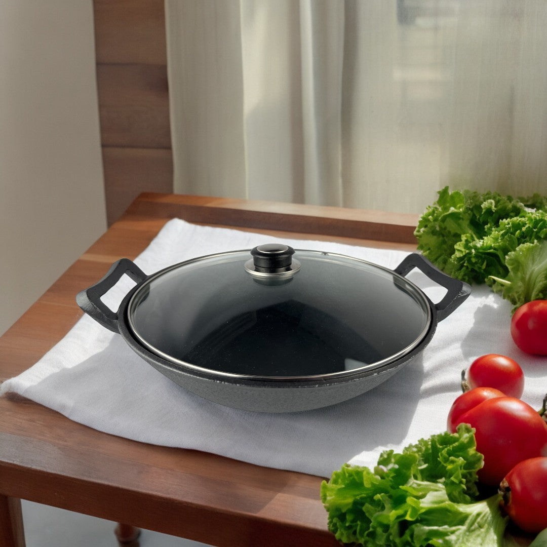Wok Ranty hierro fundido negro con tapa de vidrio sobre mesa de cocina con verduras frescas.