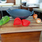 Mangos de silicona Ranty rojos en uso para wok de hierro fundido sobre tabla de corte, junto a verduras frescas.