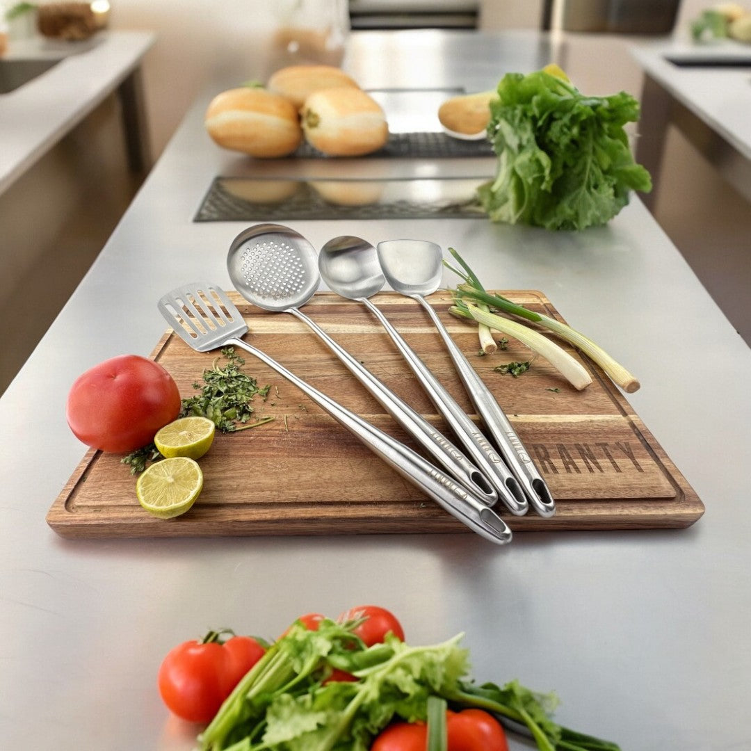 Set de 4 utensilios de cocina del chef Ranty en acero inoxidable sobre tabla de corte, trae espátulas, espumadera y cucharón.