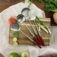 Set de 4 utensilios de cocina sostenible Ranty sobre tabla de corte, con mango de madera rojizo y acero inoxidable.