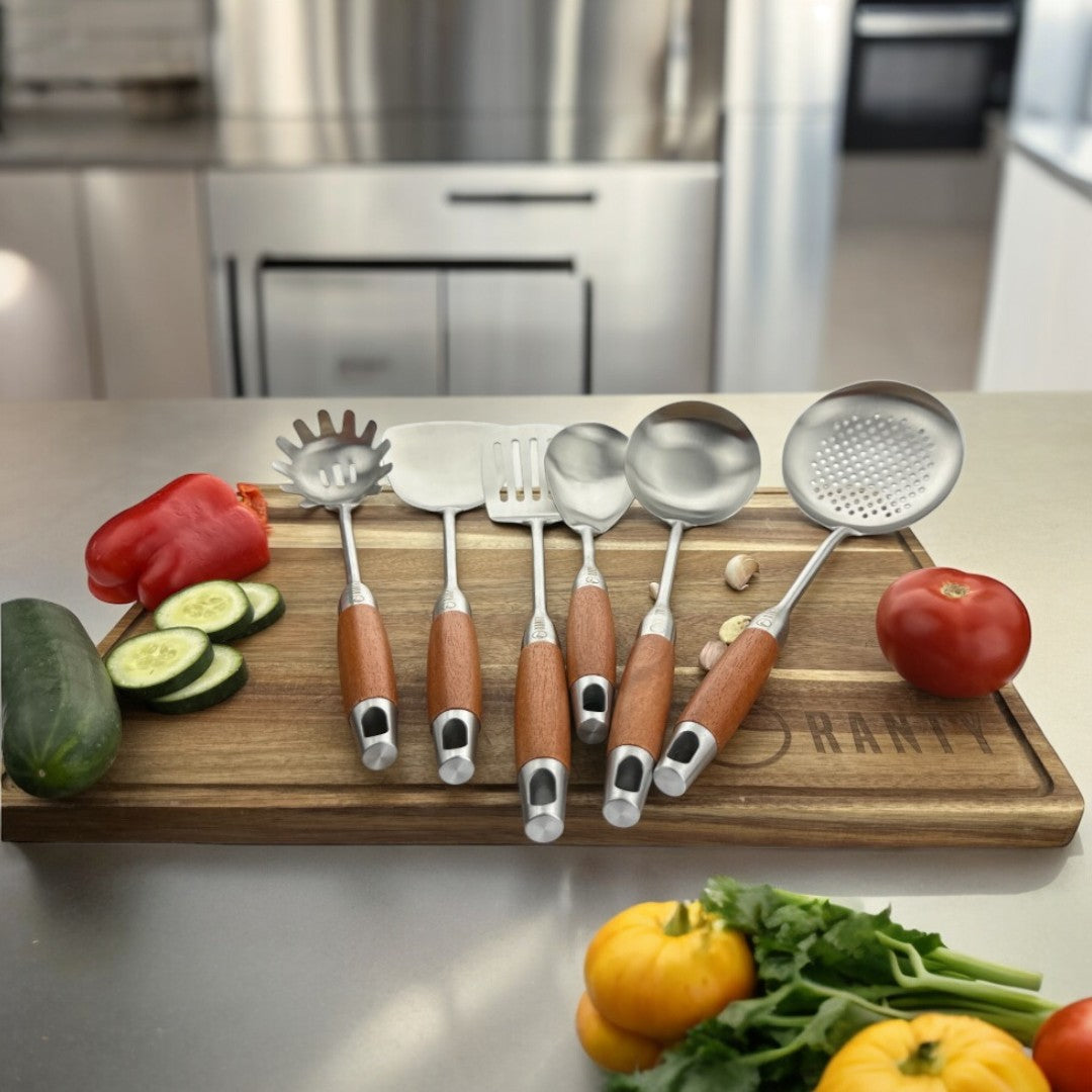 Set 6 utensilios de cocina Creativa Ranty, de acero inoxidable y mango madera  sobre tabla de cortar con verduras.