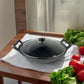Wok Ranty hierro fundido negro con tapa de vidrio sobre mesa de cocina con verduras frescas.