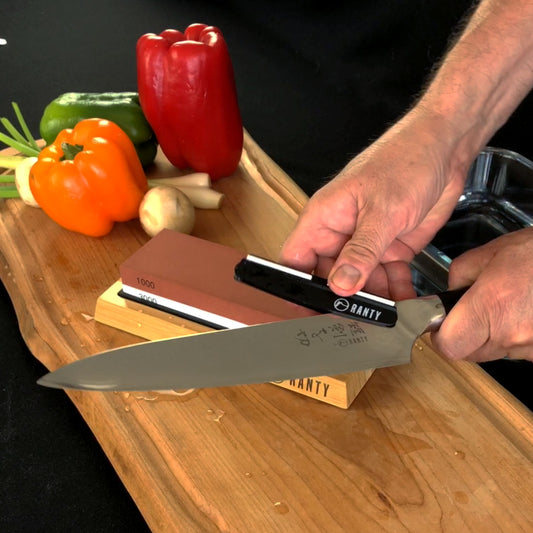 Kit afilador cuchillo piedra húmeda Ranty en uso con base antideslizante de madera de silicón sobre tabla de corte.